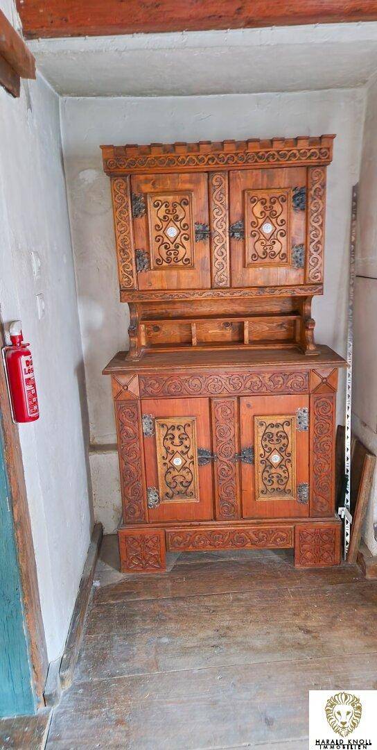 Antiker Holzschrank mit kunstvollen Schnitzereien in einem traditionellen Innenraum mit Holzboden.