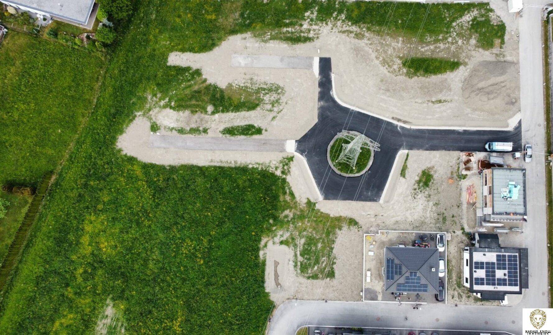 Senkrechte Luftaufnahme eines Baugebiets mit Straßen, Kreisverkehr und Häusern mit Solaranlagen auf den Dächern.