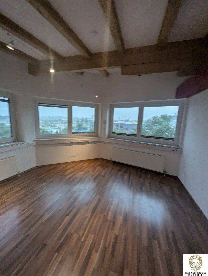 Heller Büroraum mit Holzbalkendecke und modernem Laminatboden, bietet viel natürliches Licht.