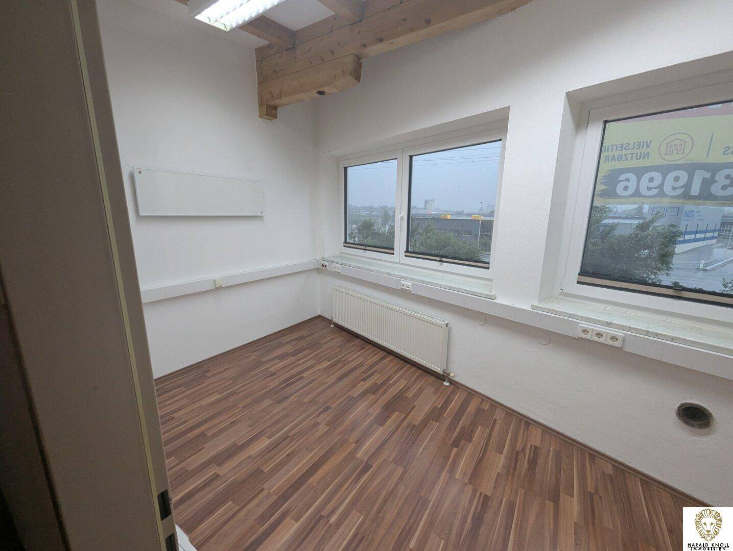 Kleineres Büro mit Laminatboden und großen Fenstern, ideal für Einzelarbeitsplätze.
