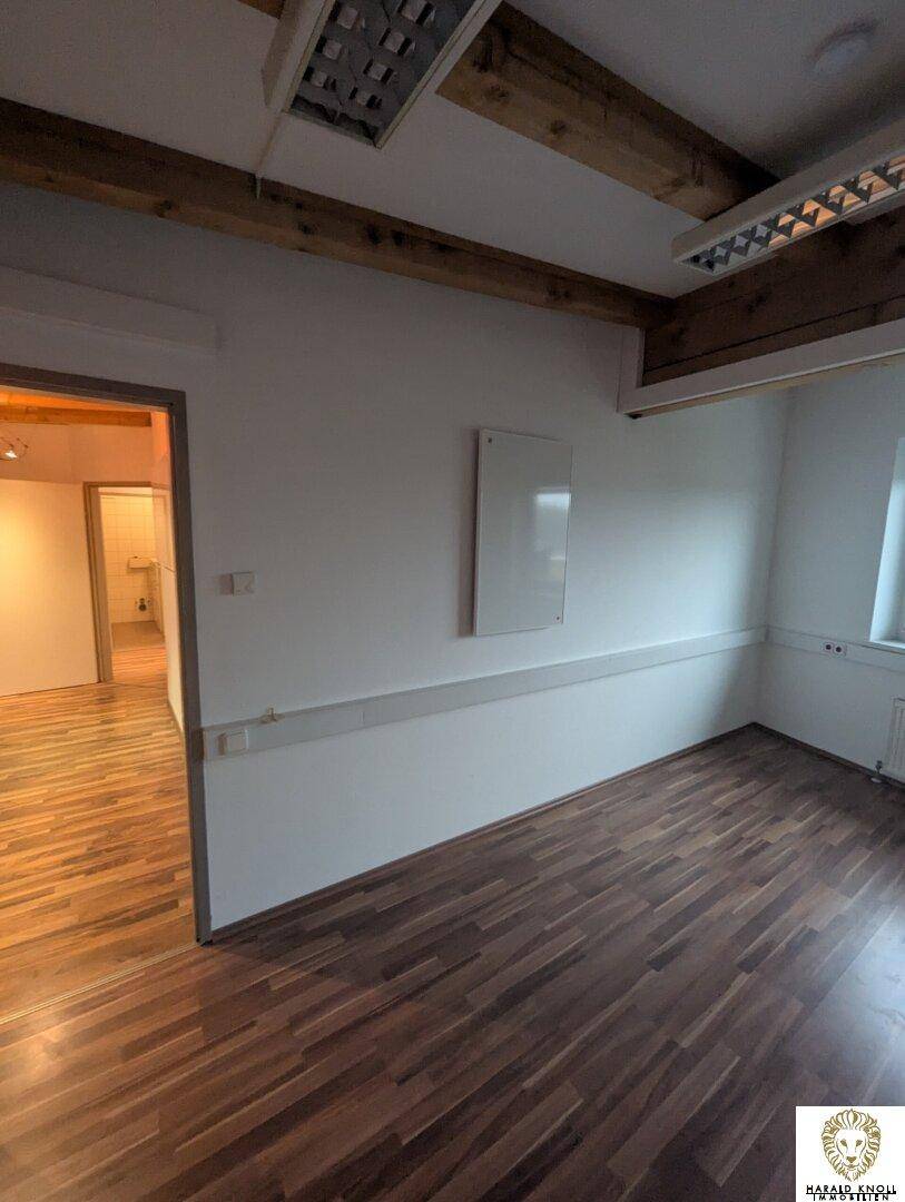 Büroraum mit Laminatboden und Blick in einen angrenzenden Bereich, möglicherweise eine Toilette.