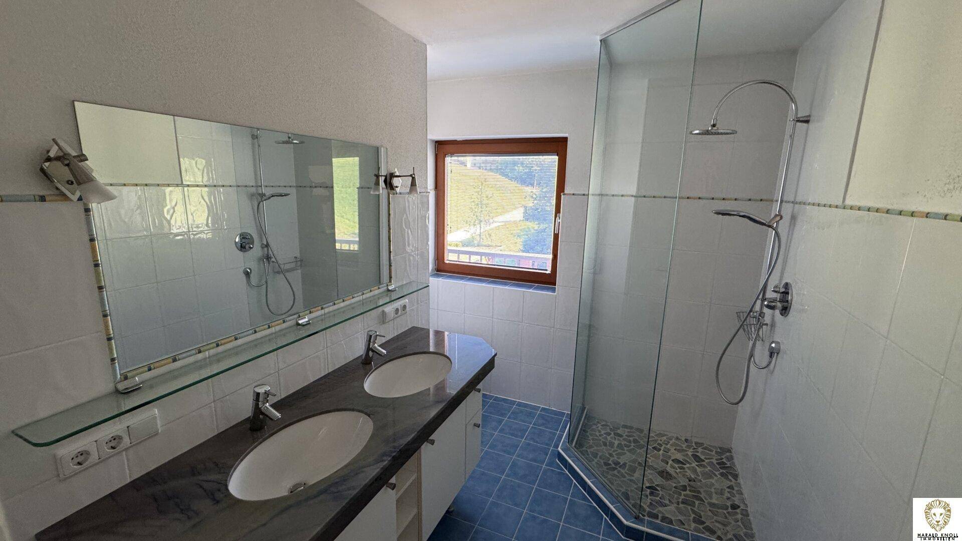 Helles Badezimmer mit Doppelwaschbecken, großer Dusche und Fenster mit Ausblick.
