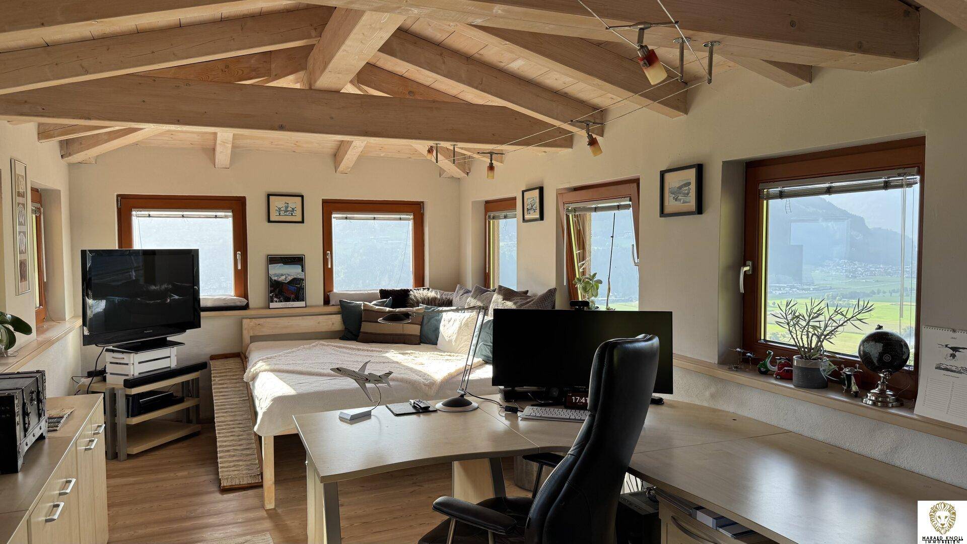 Geräumiges Schlafzimmer mit sichtbaren Holzbalken, vielen Fenstern und Bergblick.