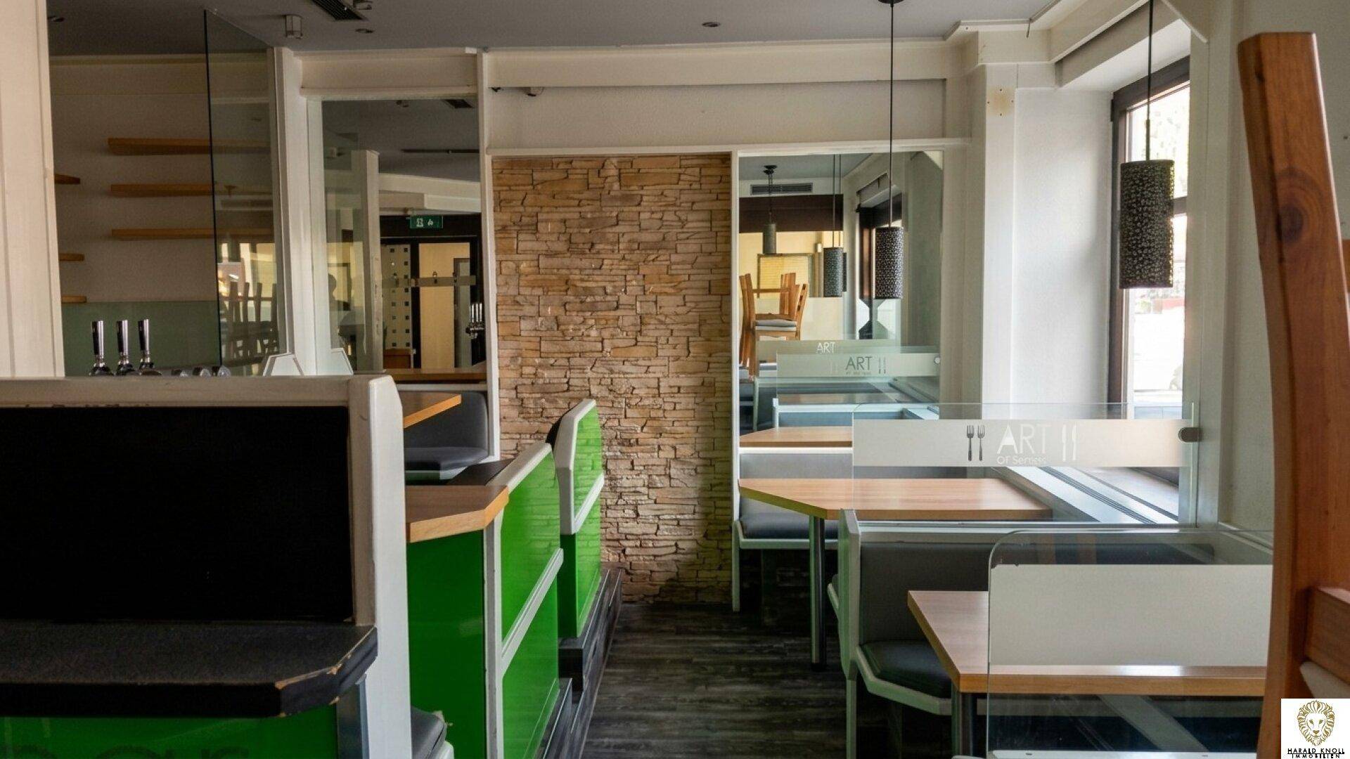 Innenbereich eines Cafés mit Sitzbänken, Holztischen und einer Wandverkleidung aus Naturstein.