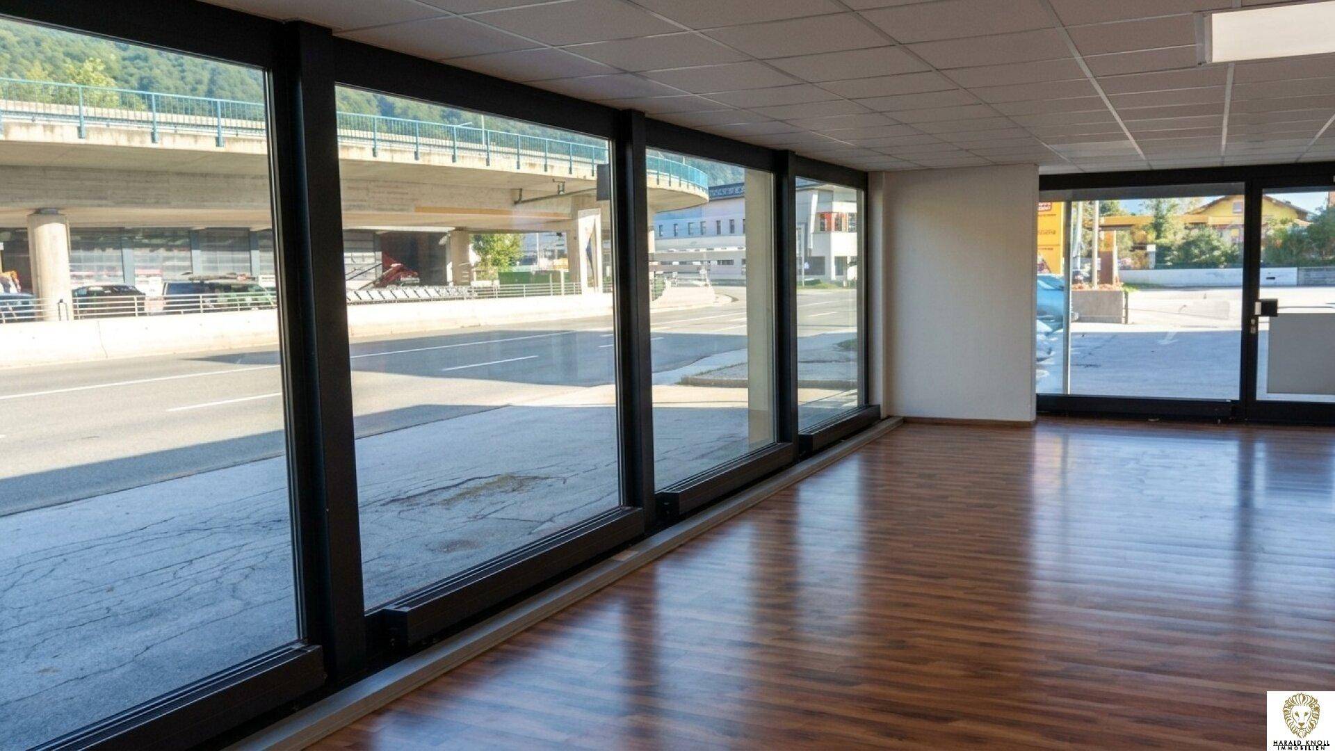 Heller Innenraum eines Geschäfts mit großen Fenstern, die auf eine Straße und eine Überführung blicken.