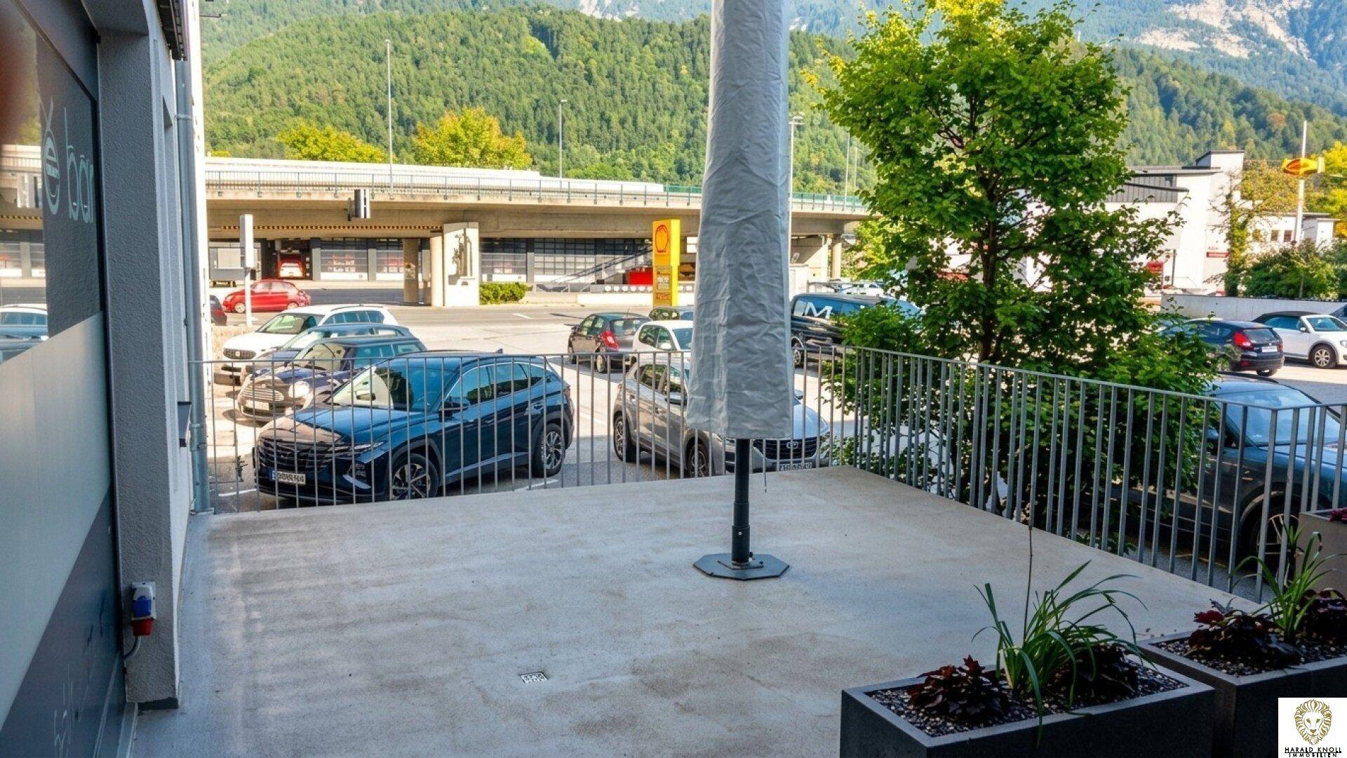 Gepflasterte Außenterrasse mit Blick auf einen Parkplatz und die umliegende Berglandschaft.