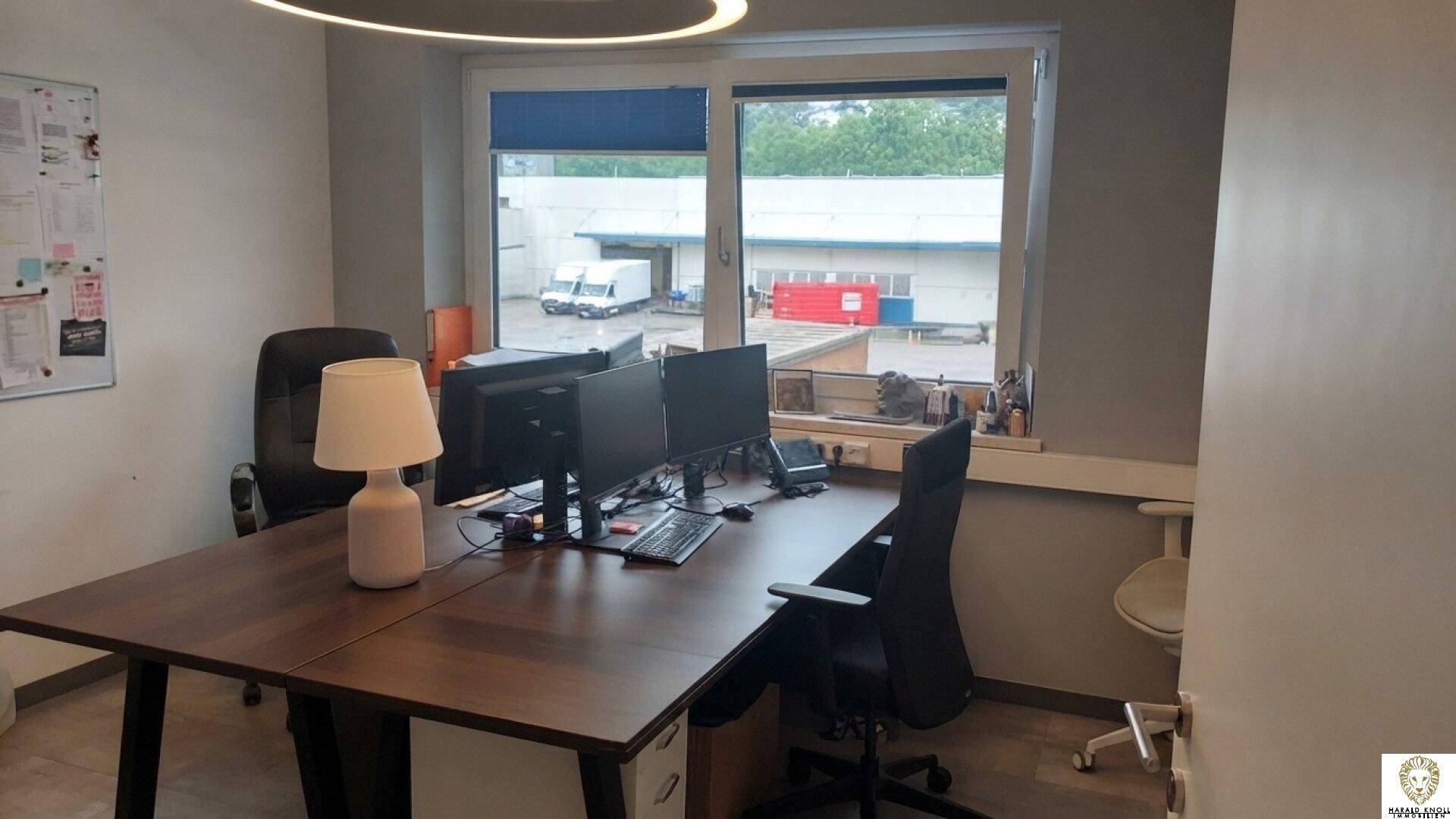 Arbeitsplatz in einem Büro mit Holzschreibtisch, Computermonitoren und einer modernen Tischlampe.