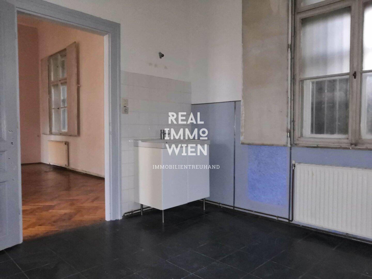 Einfacher Raum mit dunklen Fliesen, einem Waschbecken und einem Fenster, ideal als Hauswirtschaftsraum.