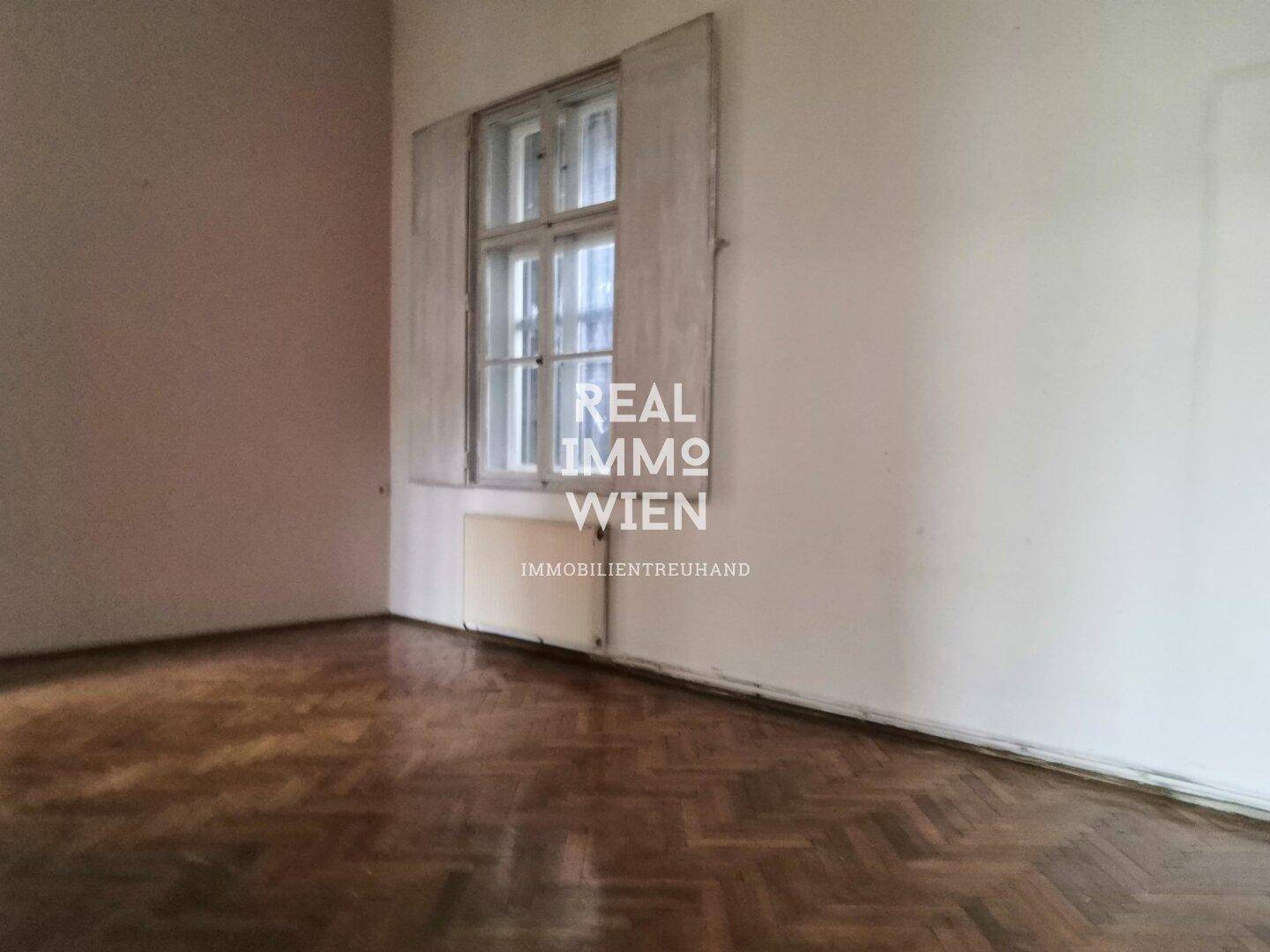 Gemütliche Ecke eines Zimmers mit Fischgrätparkett, einem großen Fenster und traditionellen Fensterläden.