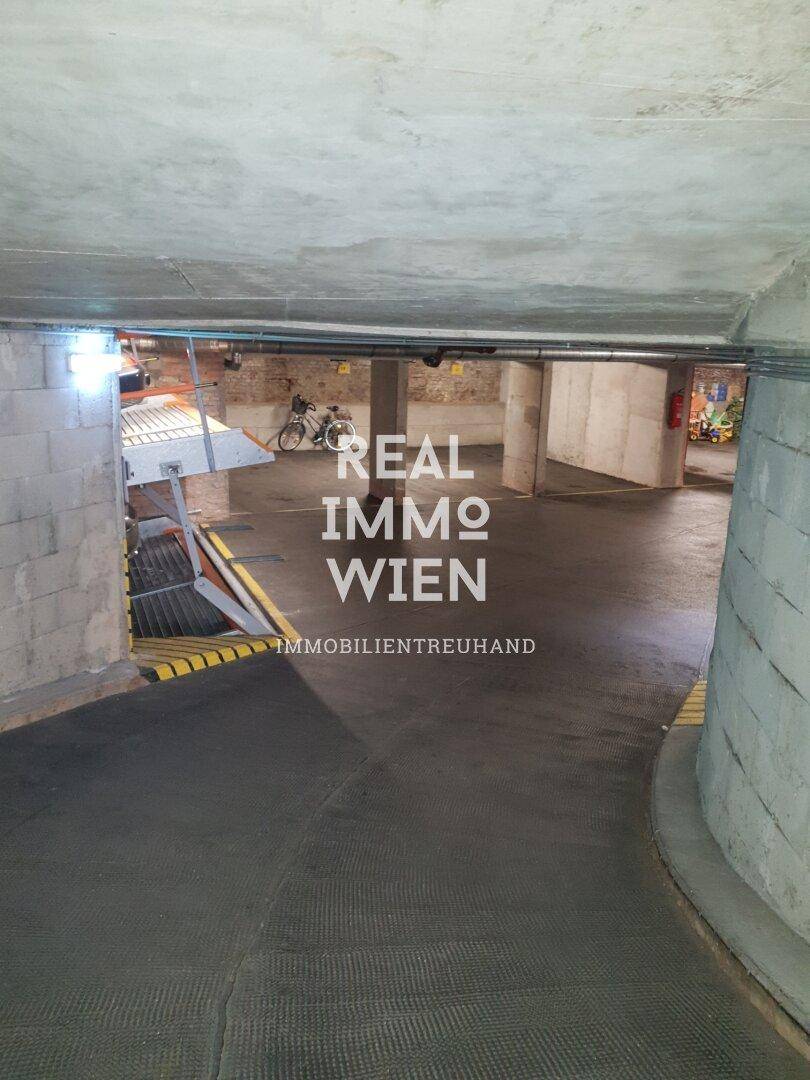 Geräumige Tiefgarage mit Zufahrtsrampe, Betonstruktur und Abstellmöglichkeiten, inklusive Fahrrad.