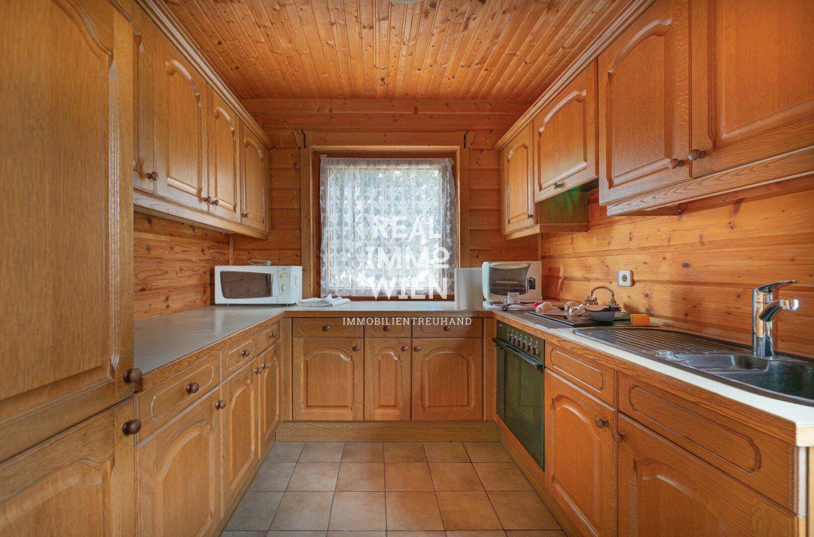 Funktionale Küche mit Holzschränken, Fliesenboden und Fenster.