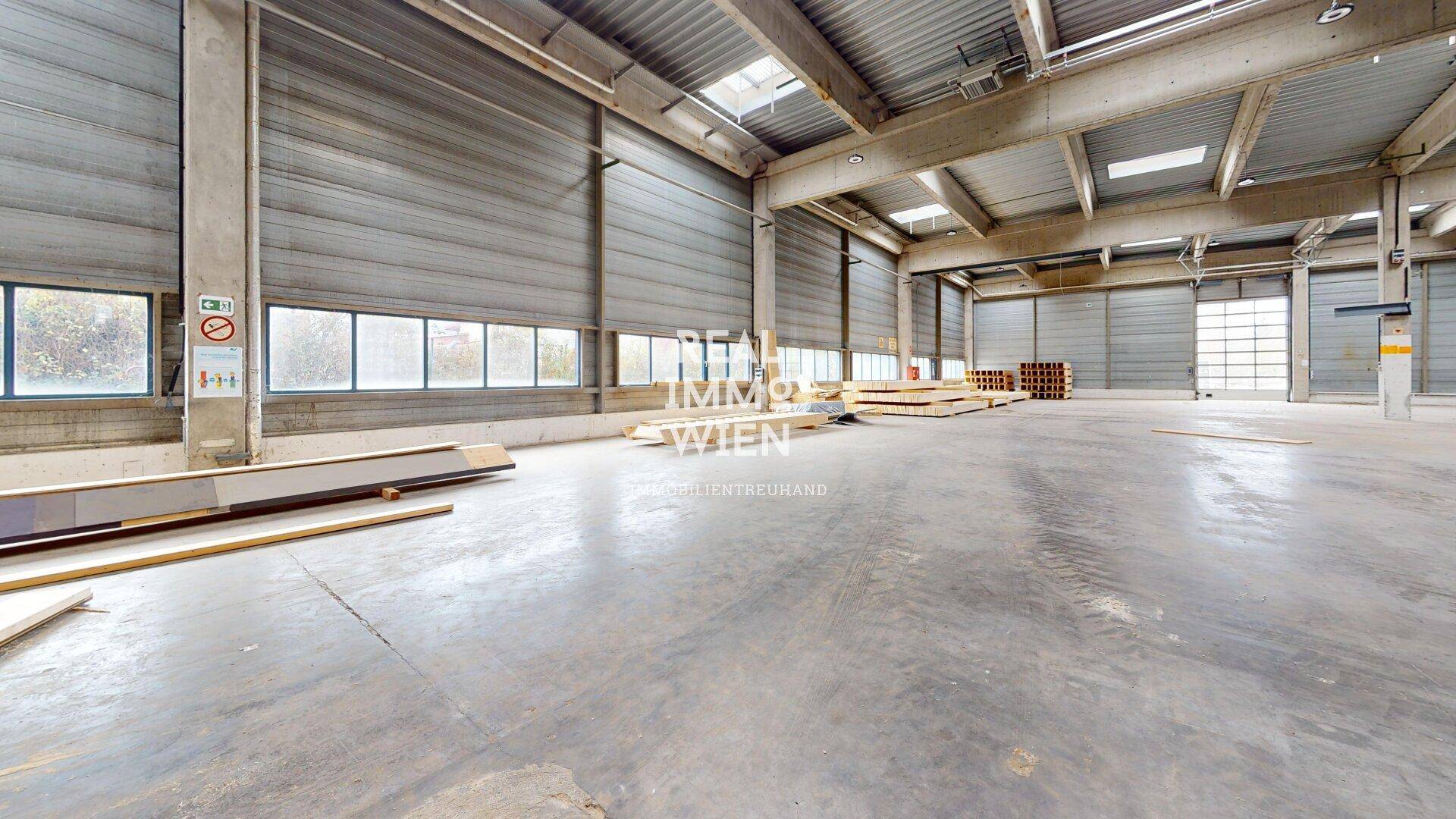 Geräumige Lagerhalle mit Betonboden, hohen Decken, Fenstern und mehreren Rolltoren.