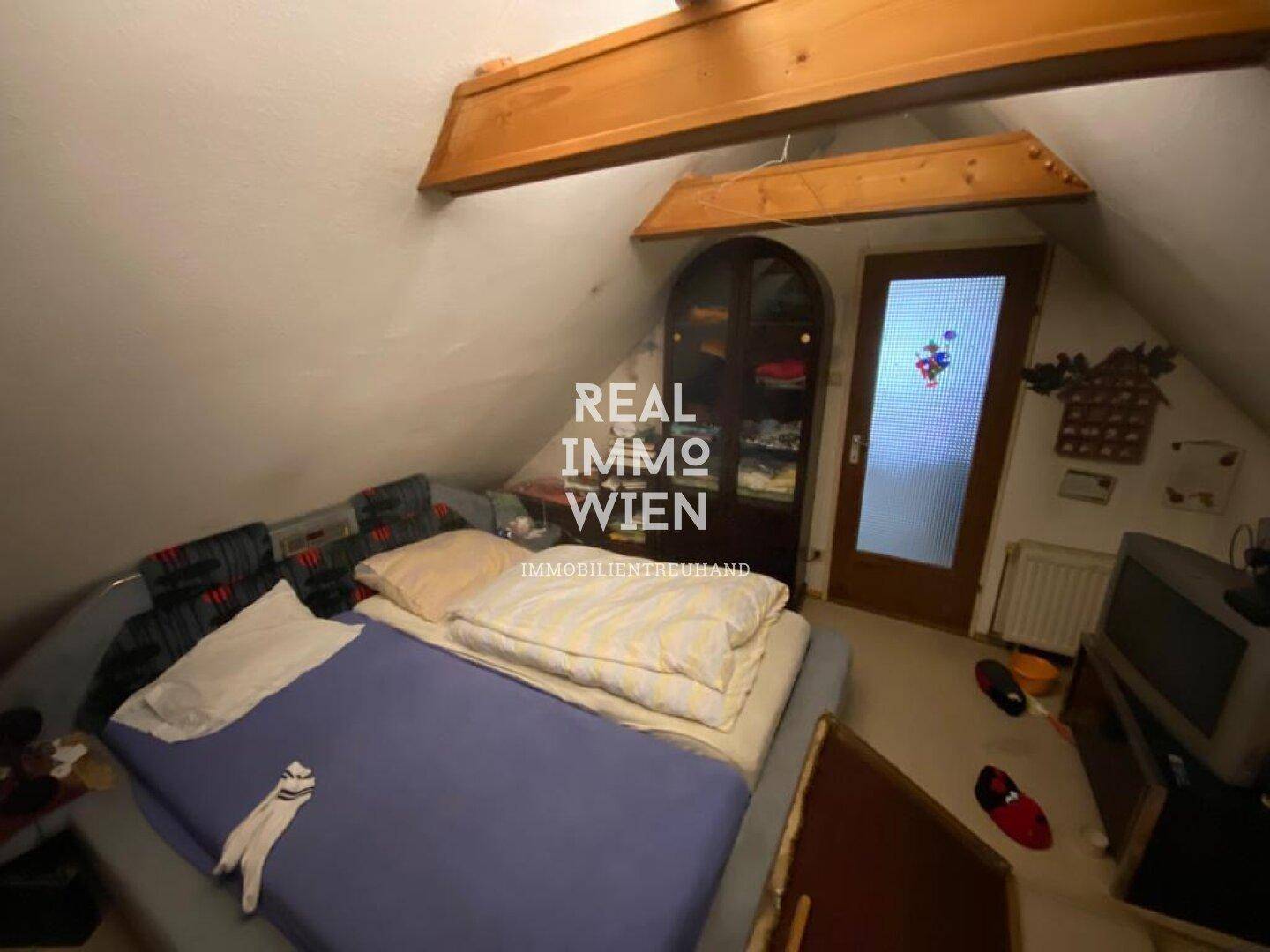 Weiteres Dachgeschosszimmer mit Bett, Schrank und schrägen Wänden unter dem Dach.