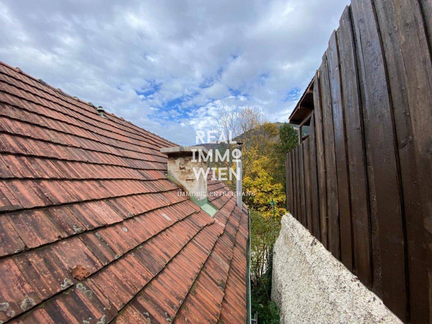 Nahaufnahme des Ziegeldachs und einer Holzwand unter bewölktem Himmel.