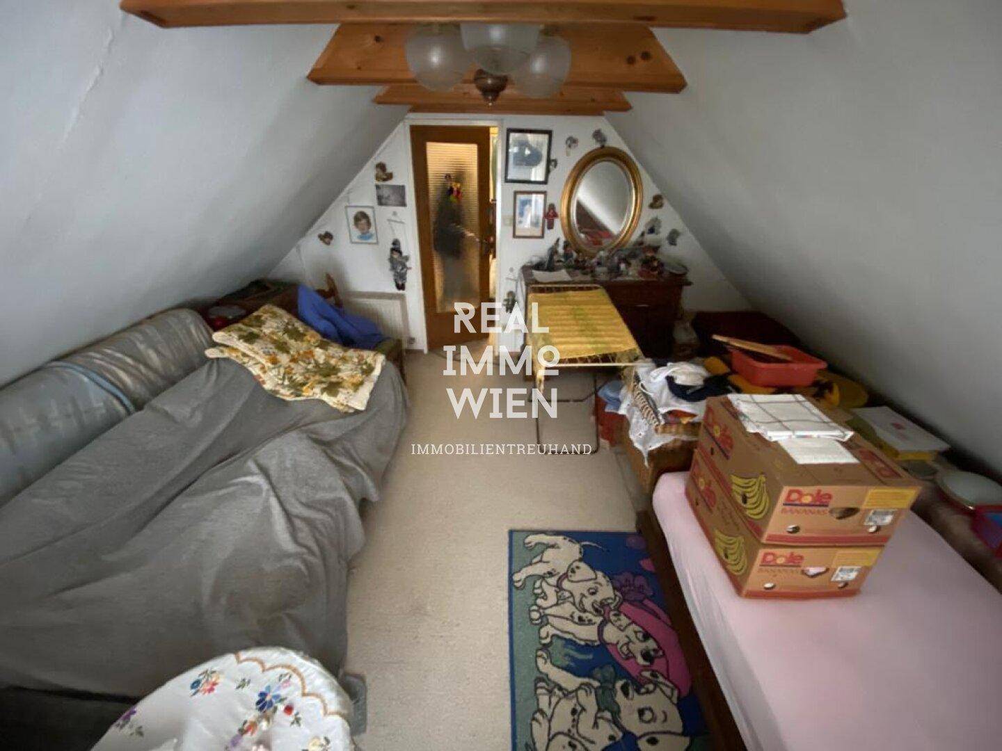 Dachgeschosszimmer mit schrägen Wänden, Holzbalken und einfacher Einrichtung.