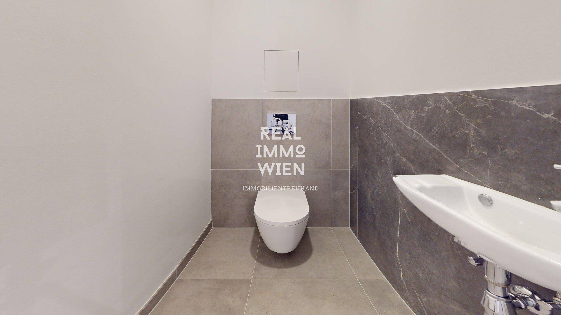 Modernes WC mit wandhängender Toilette und stilvollen grauen Fliesen an Wänden und Boden, in neuwertigem Zustand.