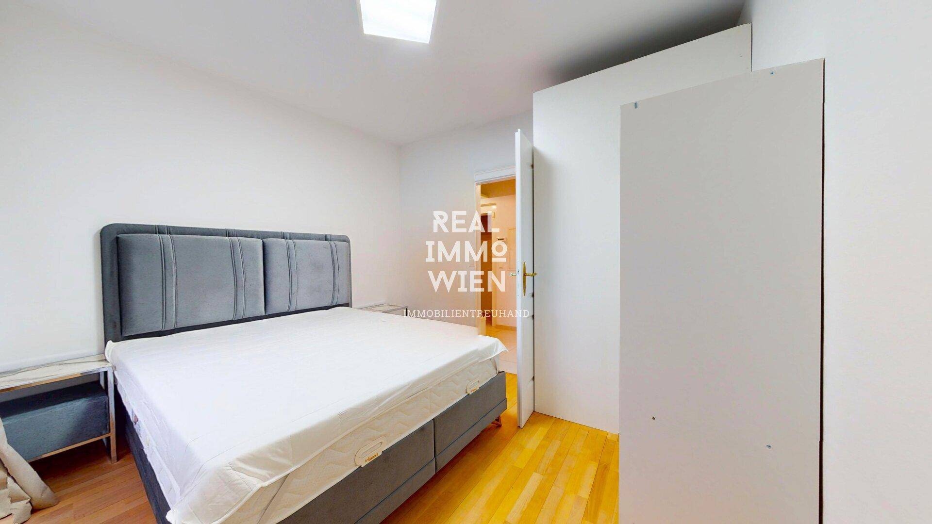 Schlafzimmer mit Doppelbett, hellem Holzboden und weißem Kleiderschrank.