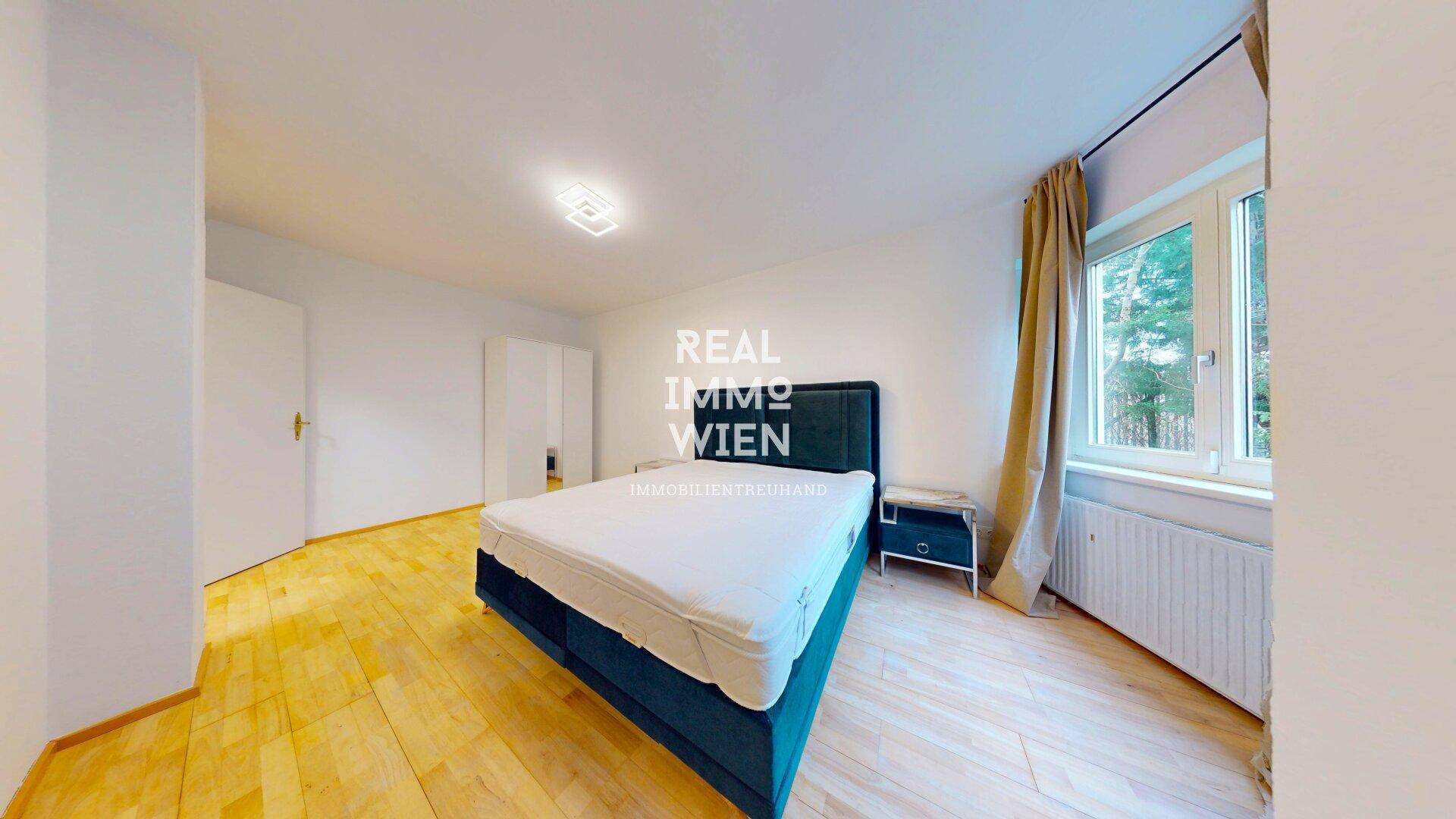 Helles Schlafzimmer mit blauem Doppelbett, Holzboden und großem Fenster.