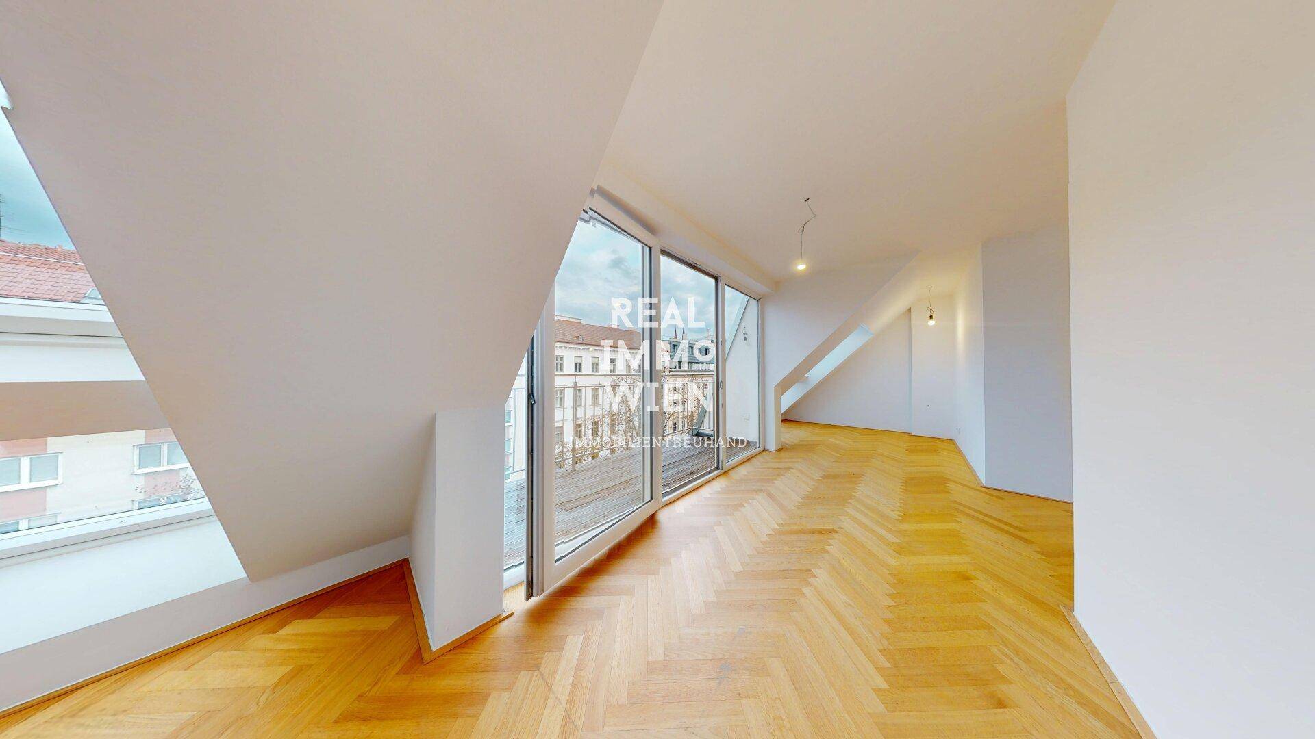 Heller Wohnbereich mit Fischgrätparkett und großen Fenstertüren, die auf den Balkon führen und viel Licht hereinlassen.