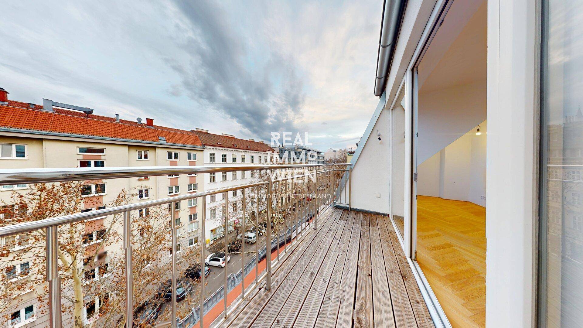 Langer Balkon mit Holzboden und Metallgeländer, bietet einen weiten Blick über die Stadt und die umliegenden Dächer.