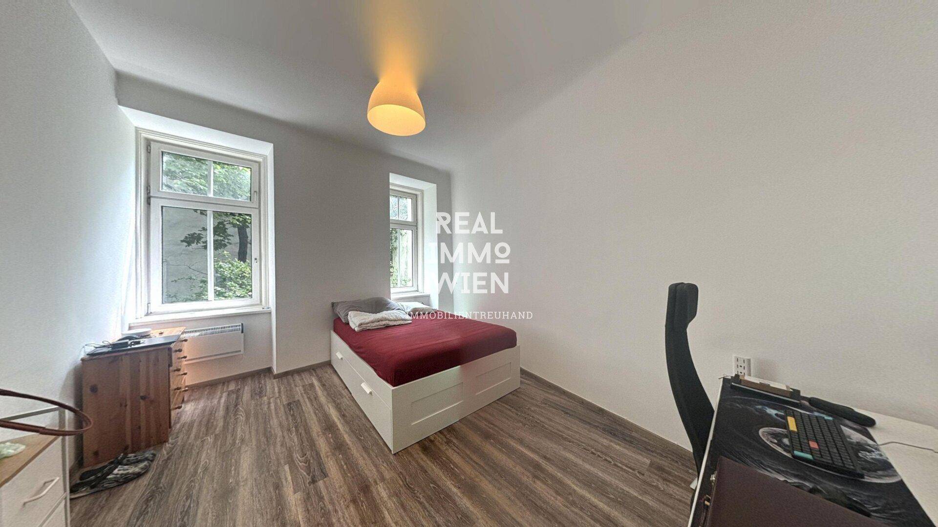 Gemütliches Schlafzimmer mit Holzboden und zwei Fenstern für natürliches Licht.