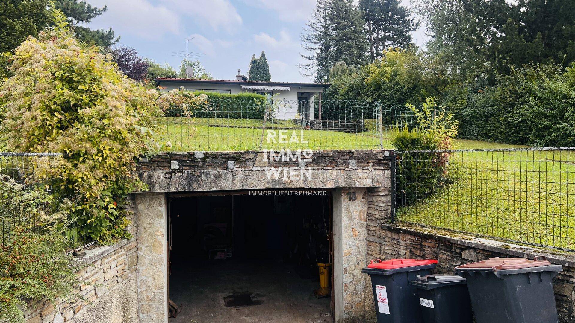 Einfahrt zur unterirdischen Garage mit robusten Steinmauern und Blick auf das darüberliegende Grundstück.