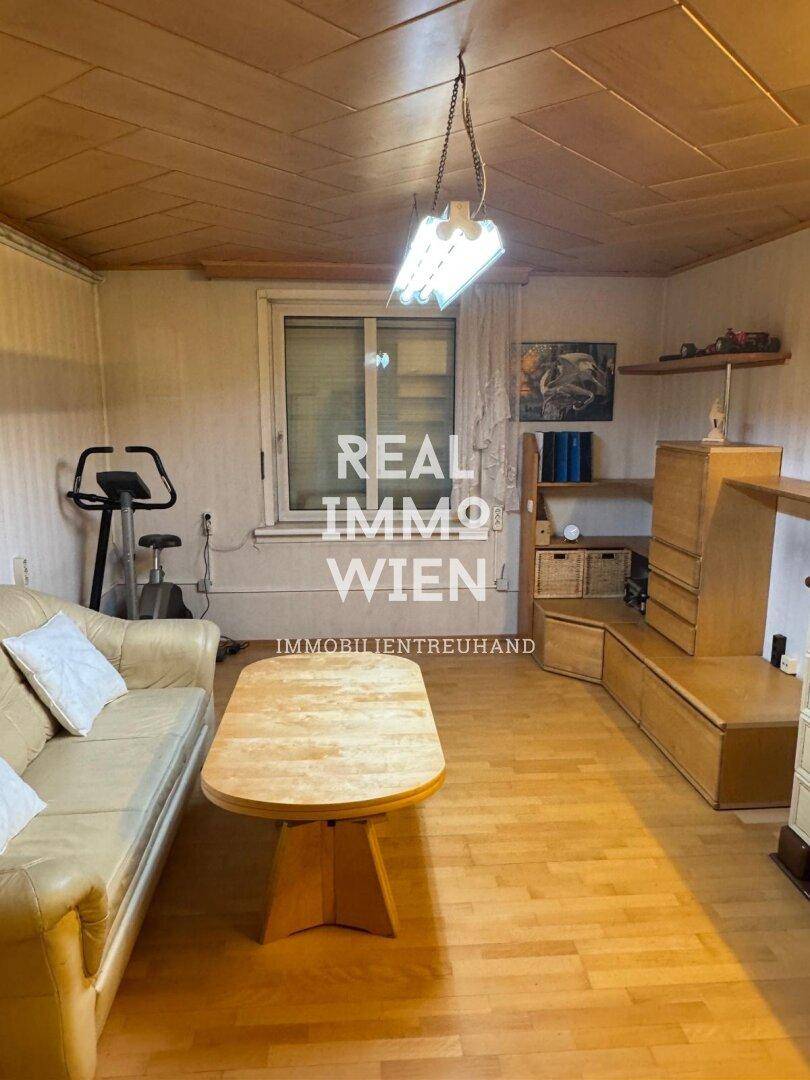 Gemütliches Wohnzimmer mit Holzdecke, Parkettboden und beiger Couch.