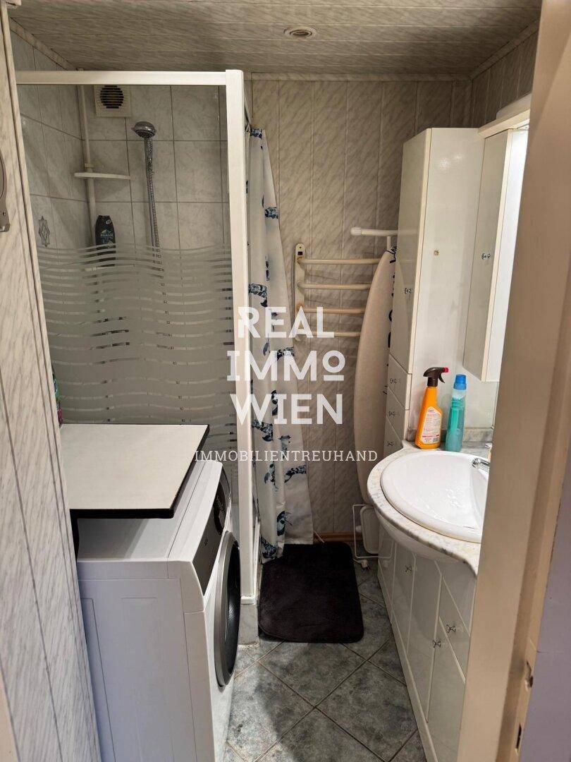 Kleines Badezimmer mit Dusche, Waschbecken und Waschmaschine.