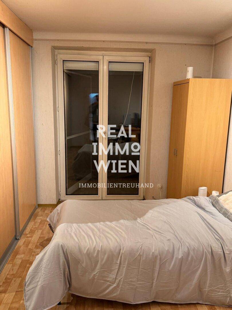 Schlafzimmer mit Doppelbett, Holzschrank und Zugang zu einem Balkon oder Terrasse.