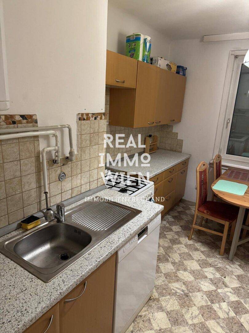 Küche mit Holzschränken, Spüle, Herd und kleinem Essbereich am Fenster.