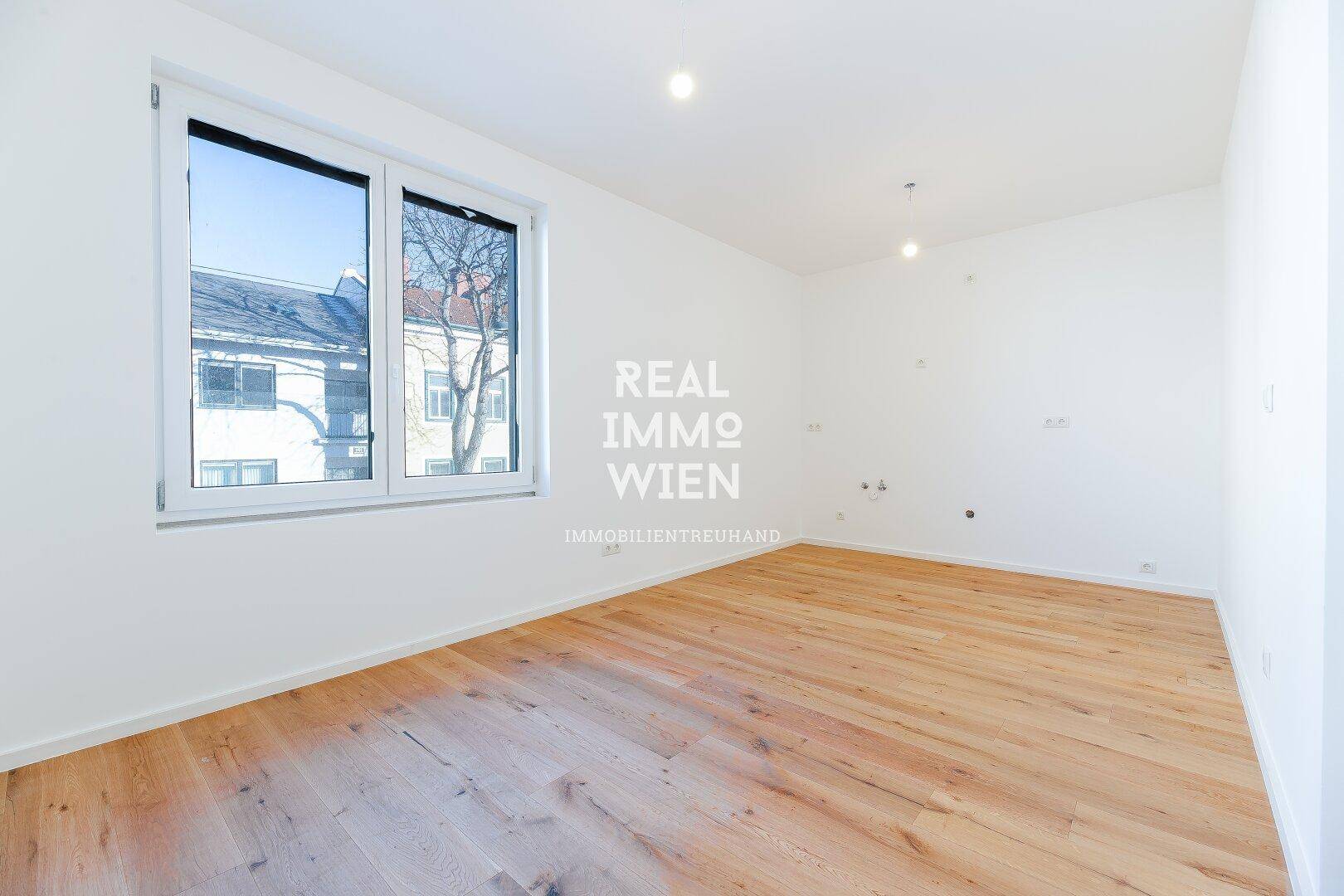 Helles, leeres Zimmer mit Holzboden und großem Fenster, ideal für Schlaf- oder Arbeitszimmer.