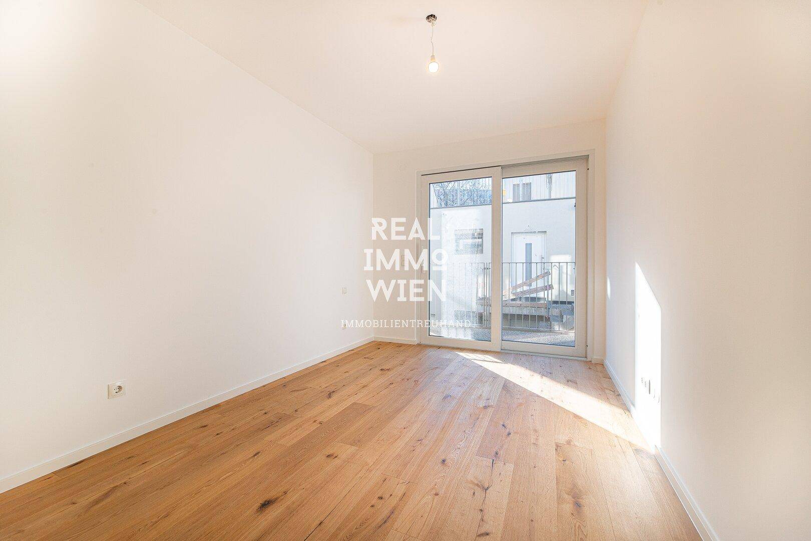 Leeres Zimmer mit hellem Holzboden und Schiebetür zum Außenbereich, ideal als Schlafzimmer.