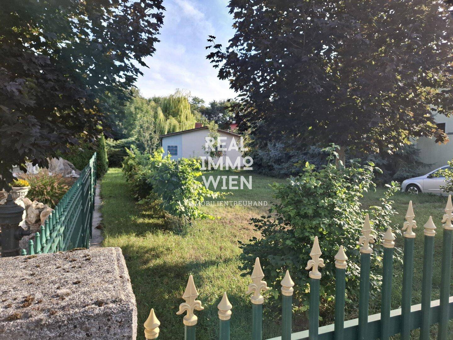 Gartenbereich mit Zaun, Bäumen und Blick auf ein kleines Gebäude.