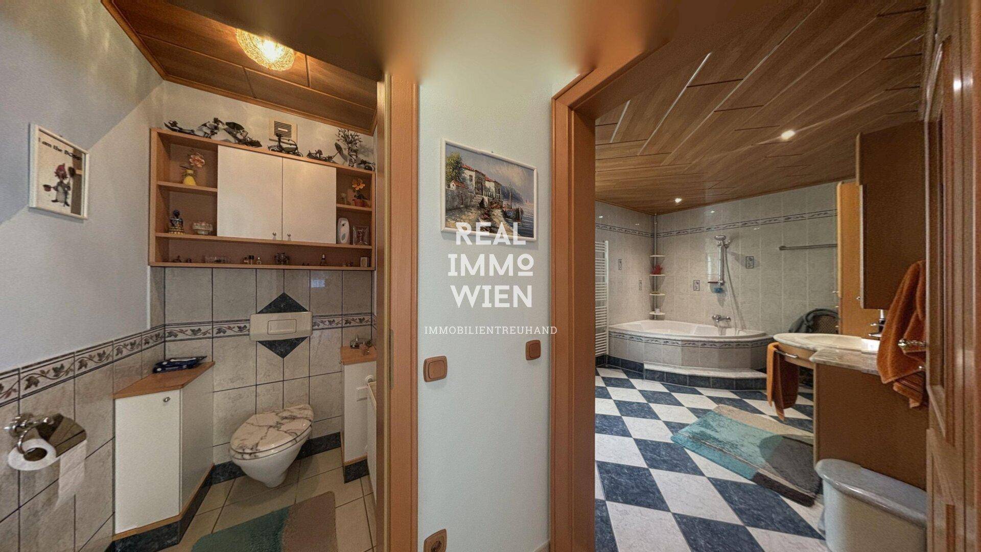 Badezimmer mit WC, Waschtisch und gefliestem Boden, angrenzend an den Hauptbadbereich.