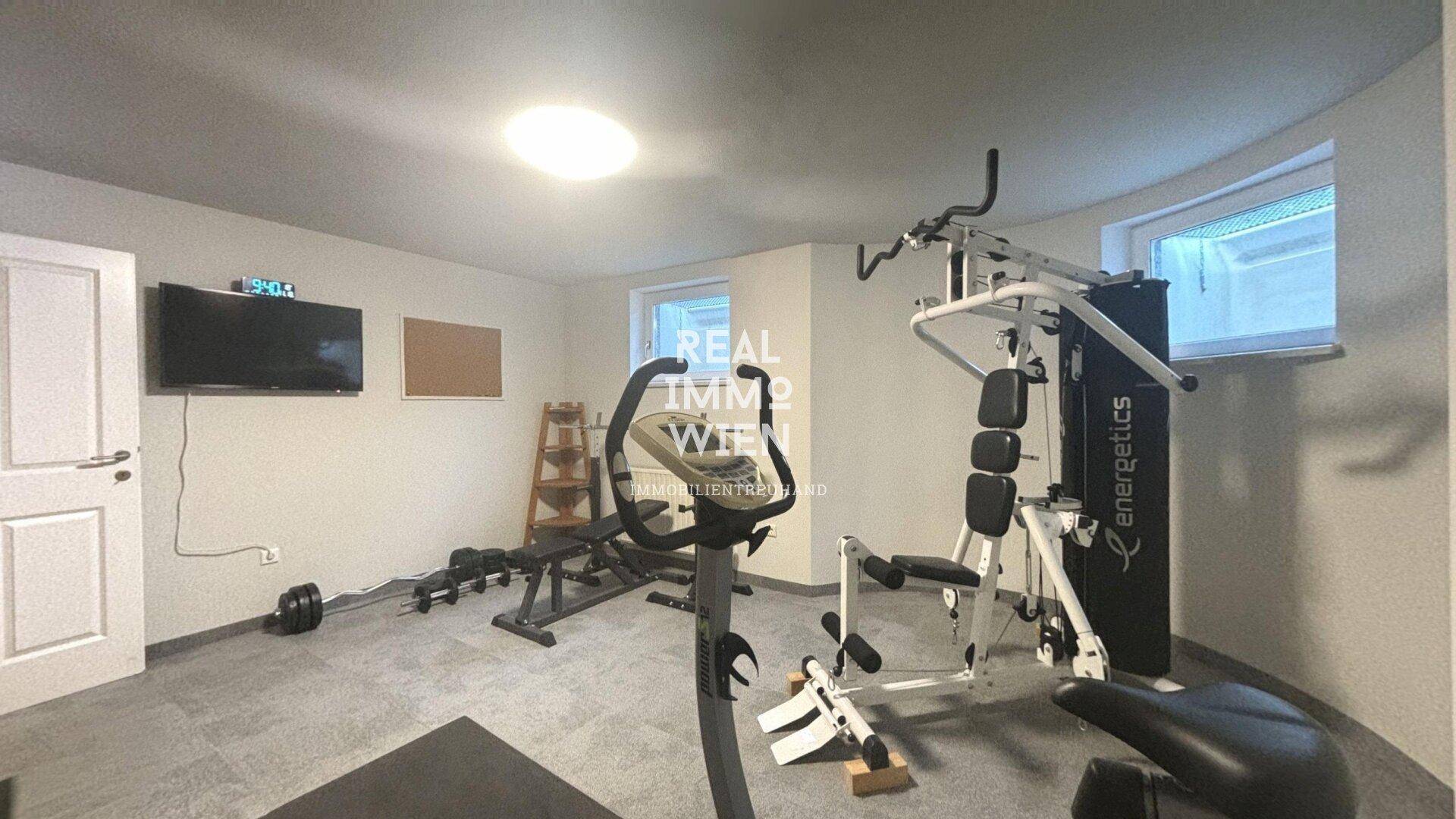 Fitnessraum im Keller mit verschiedenen Trainingsgeräten und kleinem Fenster.