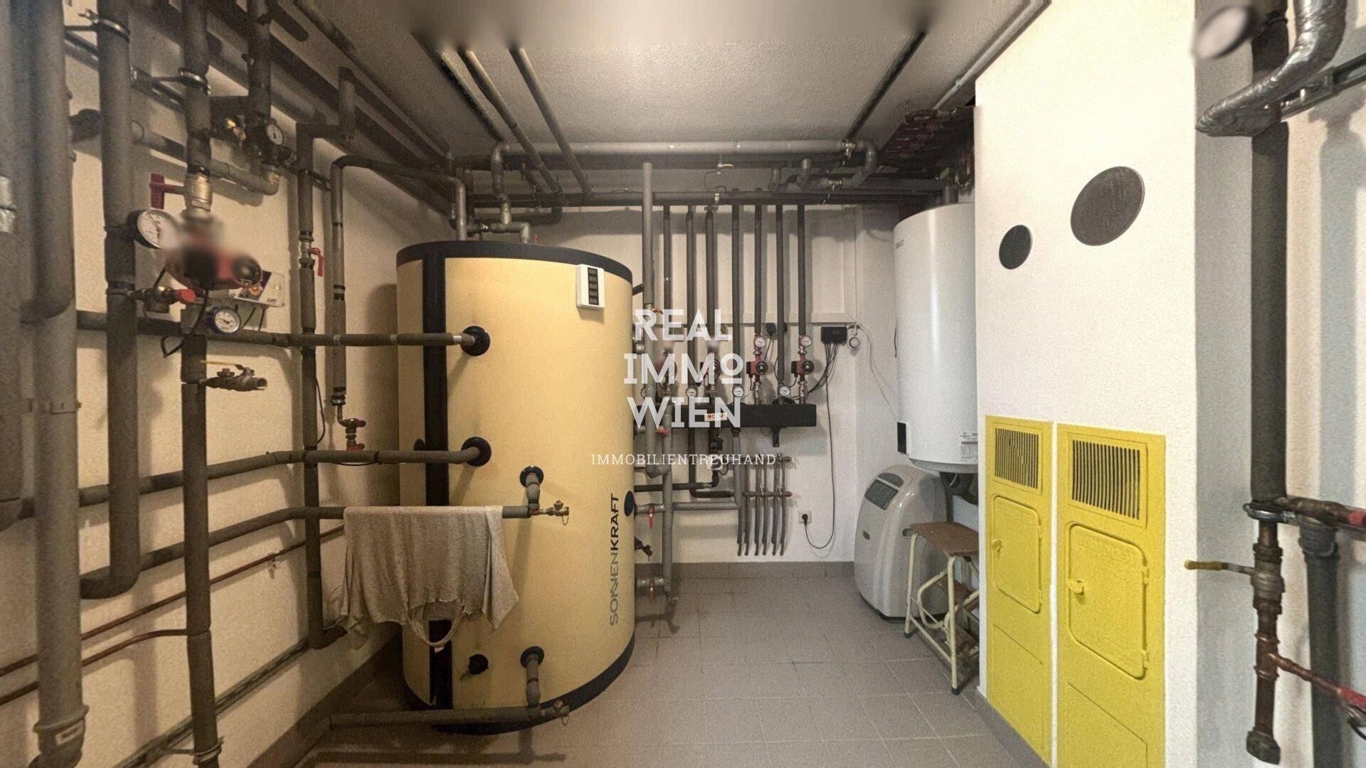 Heizungsraum im Keller mit Warmwasserspeicher und Rohrleitungen.