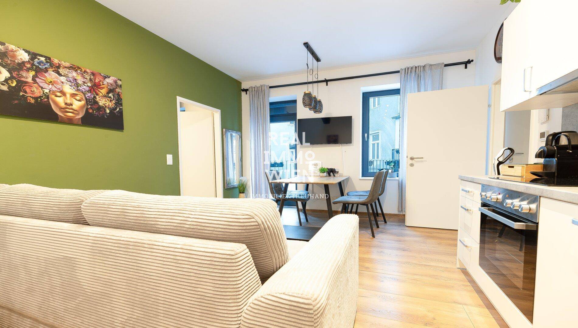 Heller Wohnbereich mit offener Küche, Esstisch und grün gestrichener Wand.
