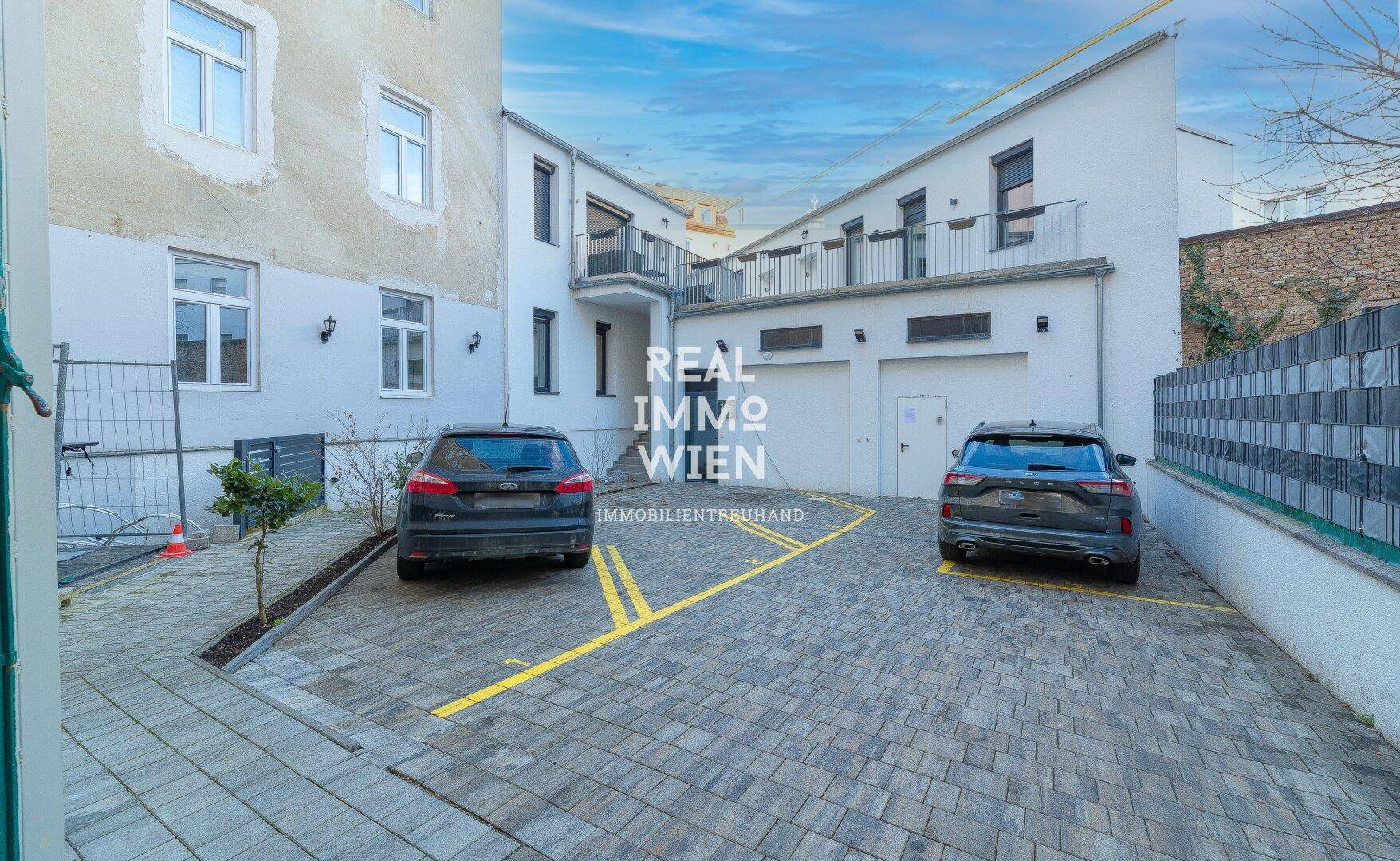 Innenhof mit gepflasterten Parkplätzen und Zugang zu Garagen.