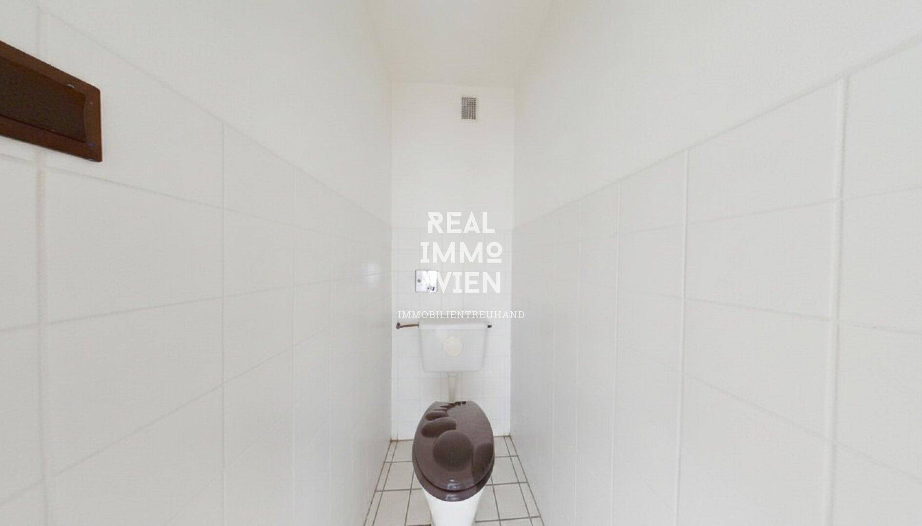 Separates WC mit weißer Fliesenverkleidung und einfacher Ausstattung.