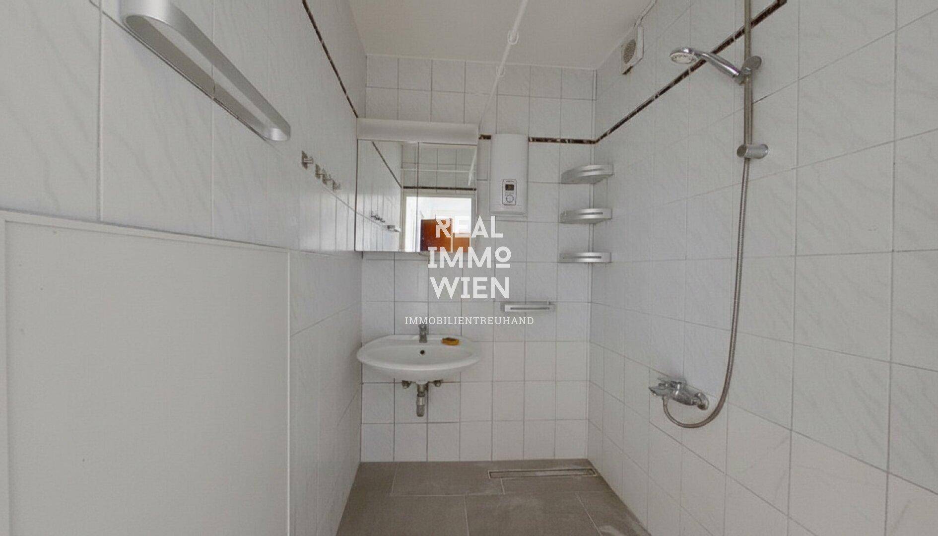 Gefliestes Badezimmer mit Dusche, Waschbecken und Spiegel, in gutem Zustand.