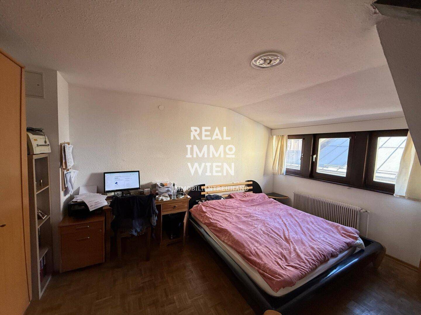 Gemütliches Schlafzimmer mit Holzboden, Dachschräge und Fensterfront für natürliches Licht.