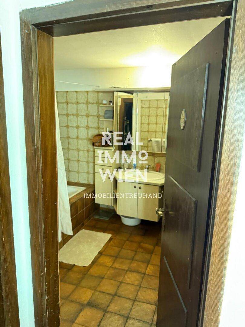 Badezimmer mit älteren Fliesen, Badewanne und Waschbecken, das Renovierungsbedarf zeigt.