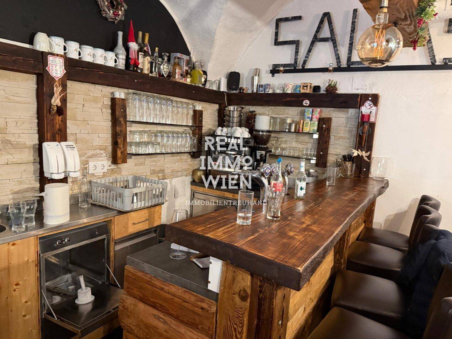Rustikale Bar mit Holztheke, Steinwandelementen und Gläserregalen in einem Gastronomiebereich.