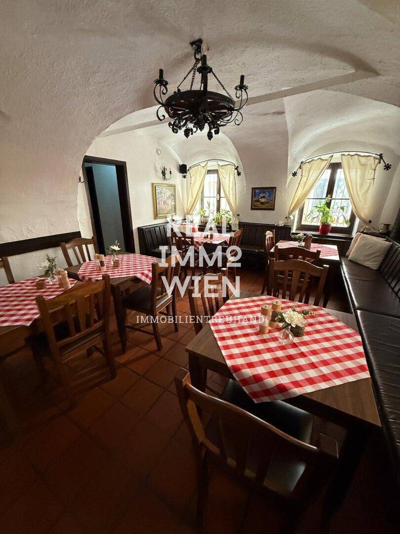 Traditioneller Gastraum mit Gewölbedecken, Holztischen und karierten Tischdecken, hell beleuchtet.