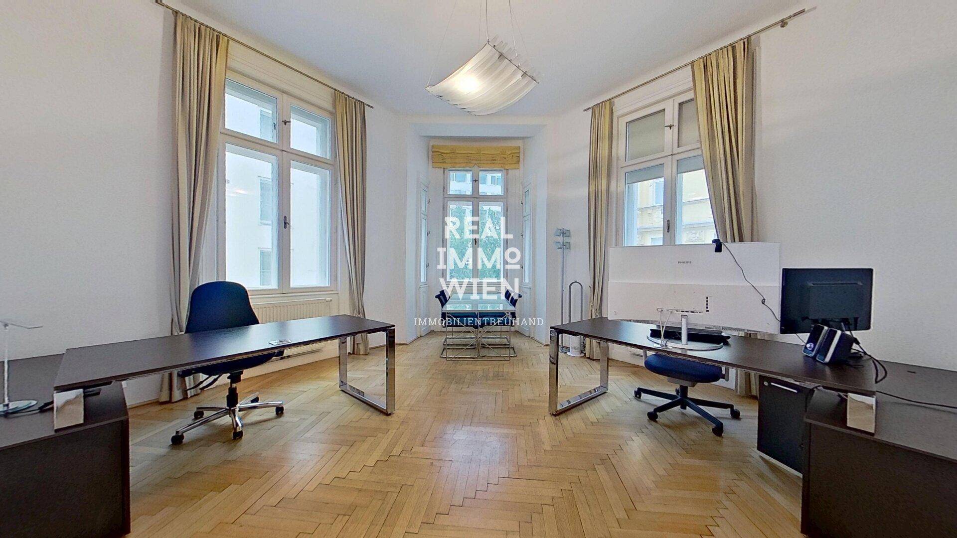 Geräumiges Büro mit zwei Arbeitsplätzen, Fischgrätparkett und hohen Fenstern, die für eine helle Atmosphäre sorgen.
