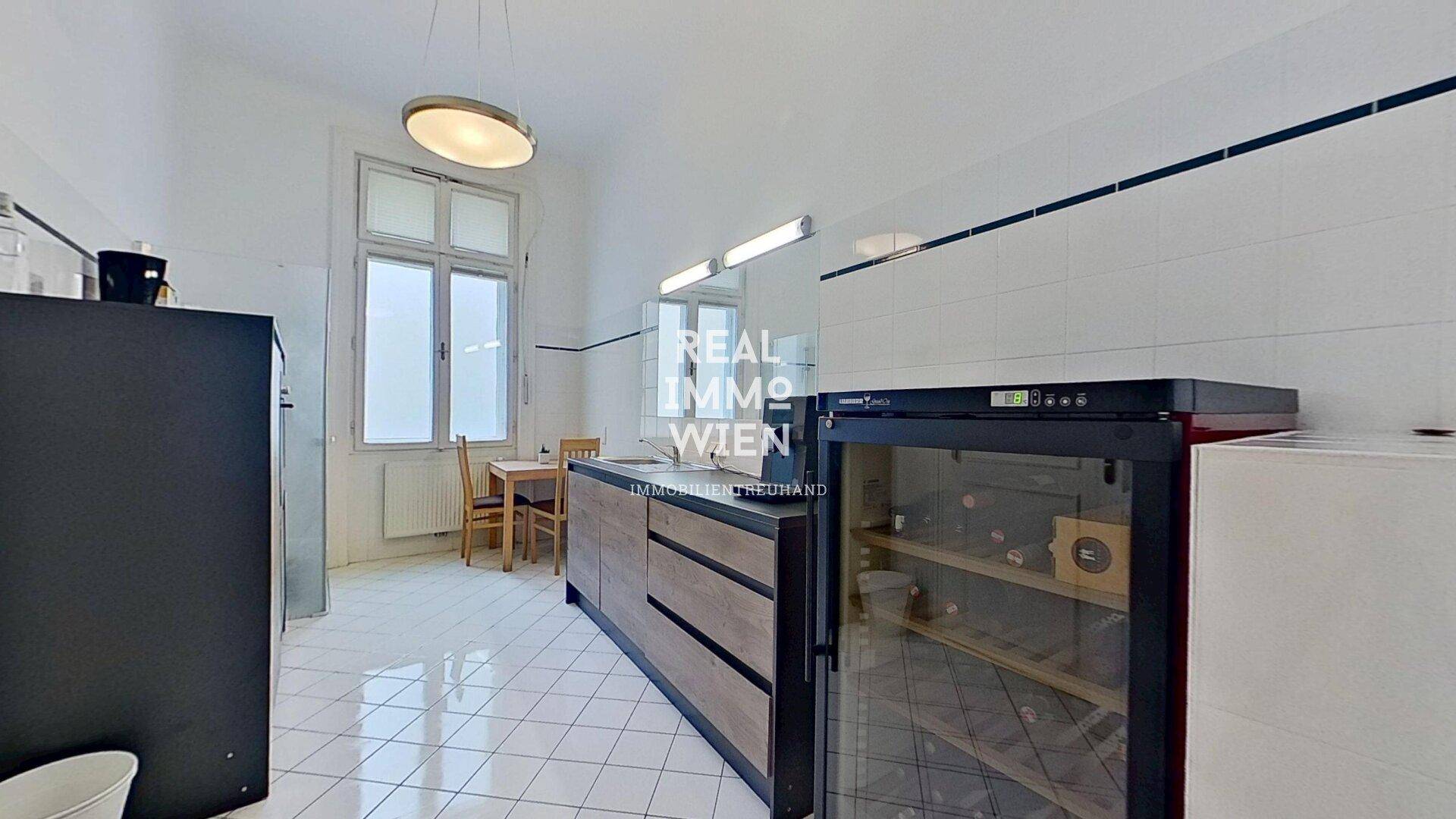 Funktionale Küche mit weißen Fliesen, Holzschränken und einem Weinkühlschrank.