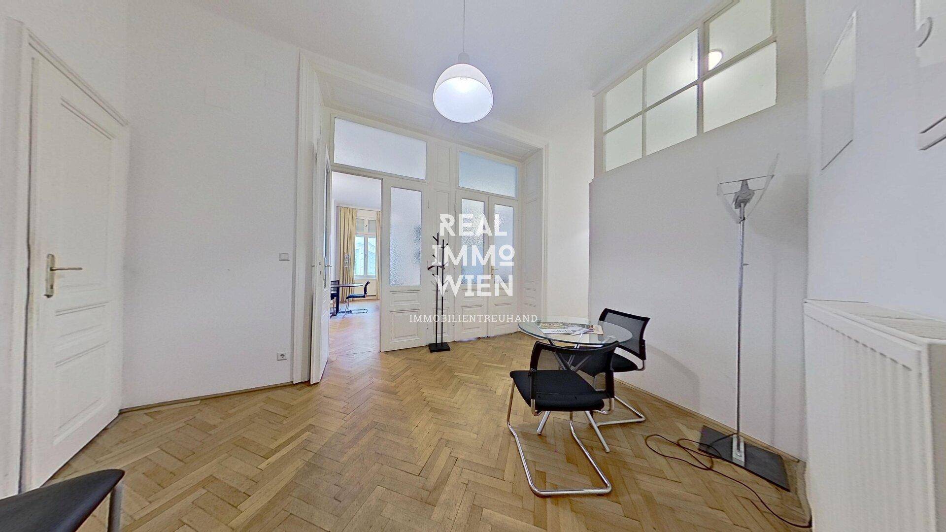 Heller Raum mit Fischgrätparkett, hohen Decken und großen Doppeltüren zu einem weiteren Zimmer.