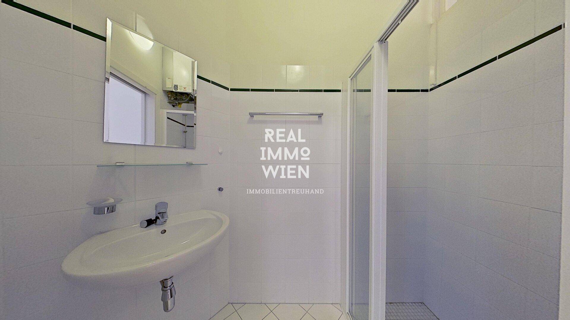 Funktionales Badezimmer mit weiß gefliesten Wänden, Waschbecken und einer Duschkabine.