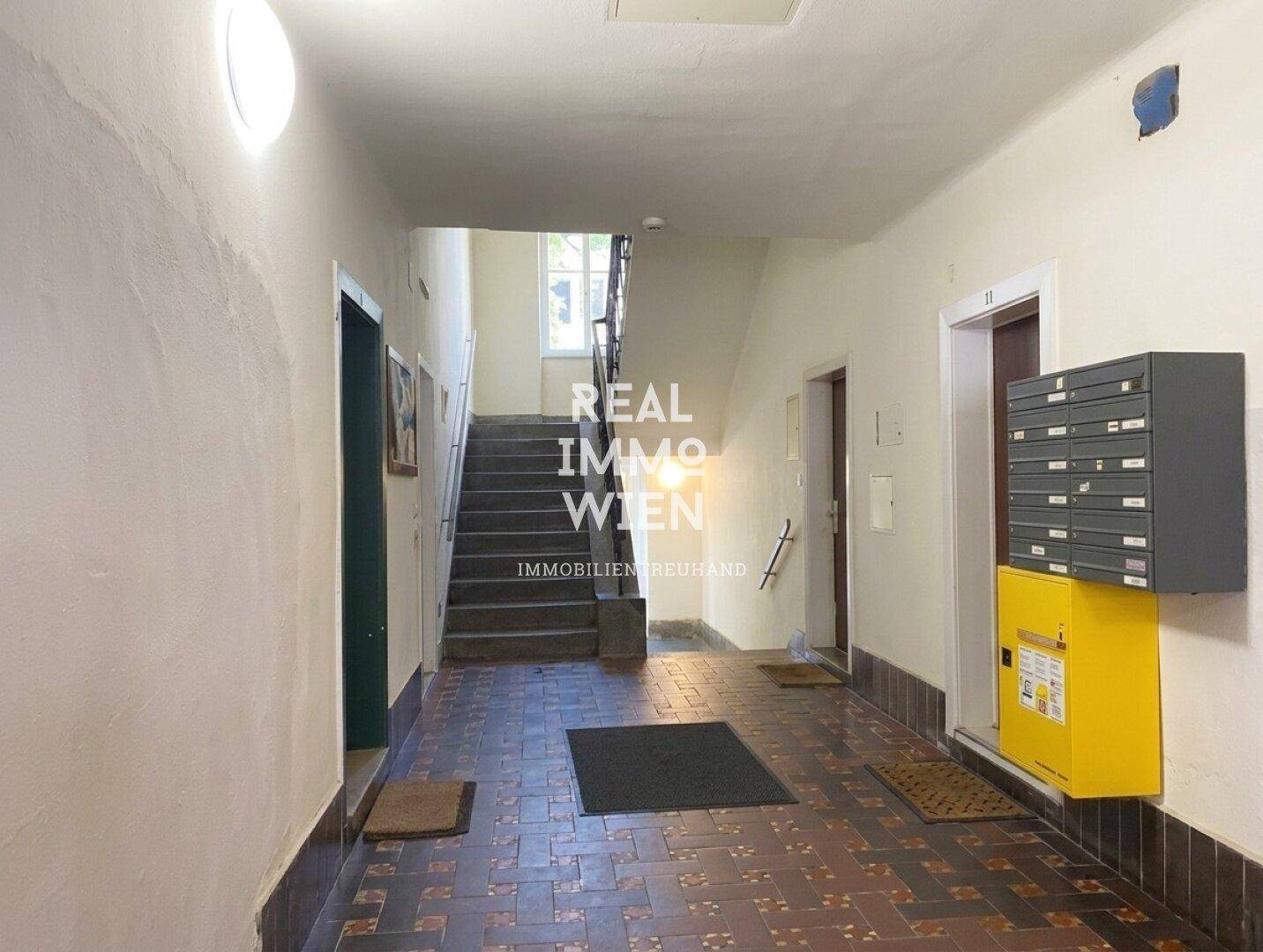 Eingangsbereich eines Mehrfamilienhauses mit Treppenaufgang, Fliesenboden und Briefkästen.