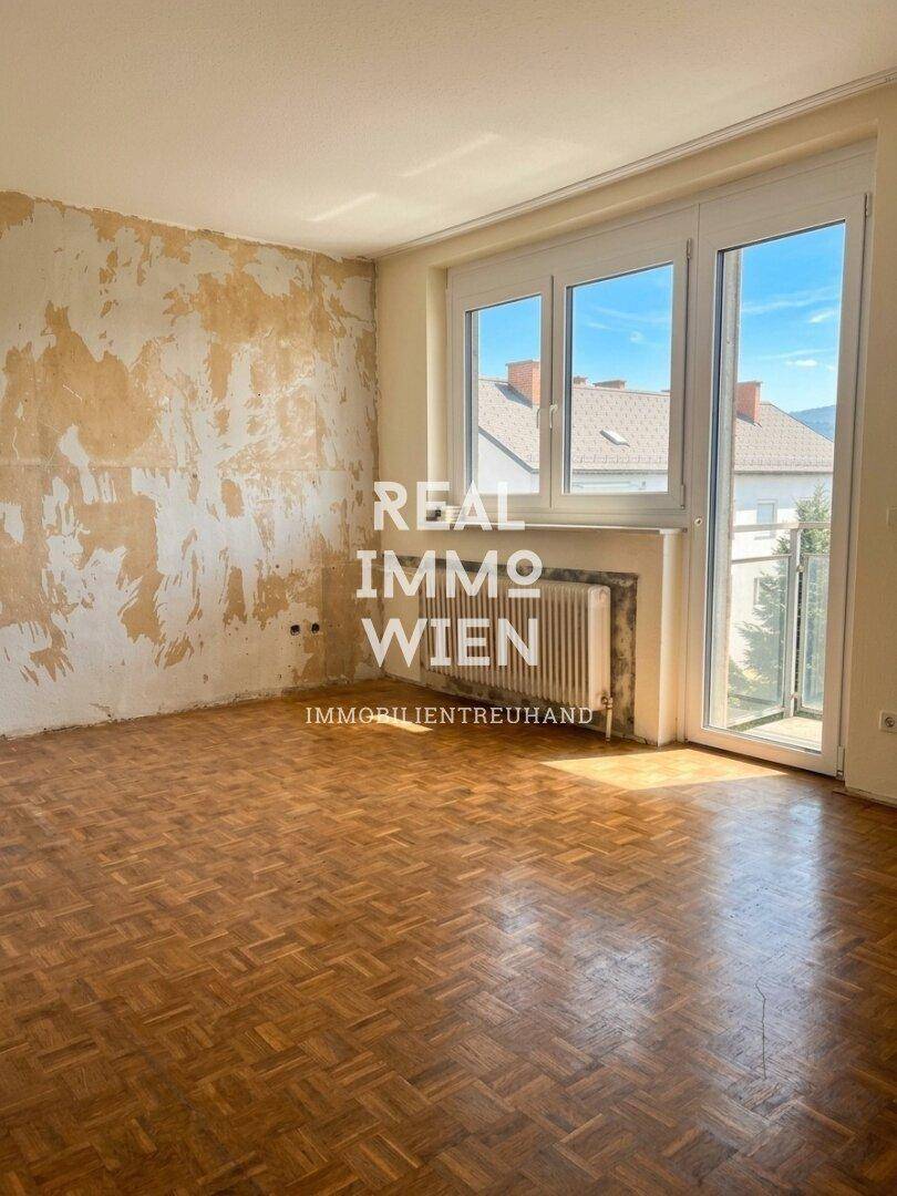 Heller Wohnraum mit Parkettboden und Zugang zu einem kleinen Balkon, bereit zur Renovierung.